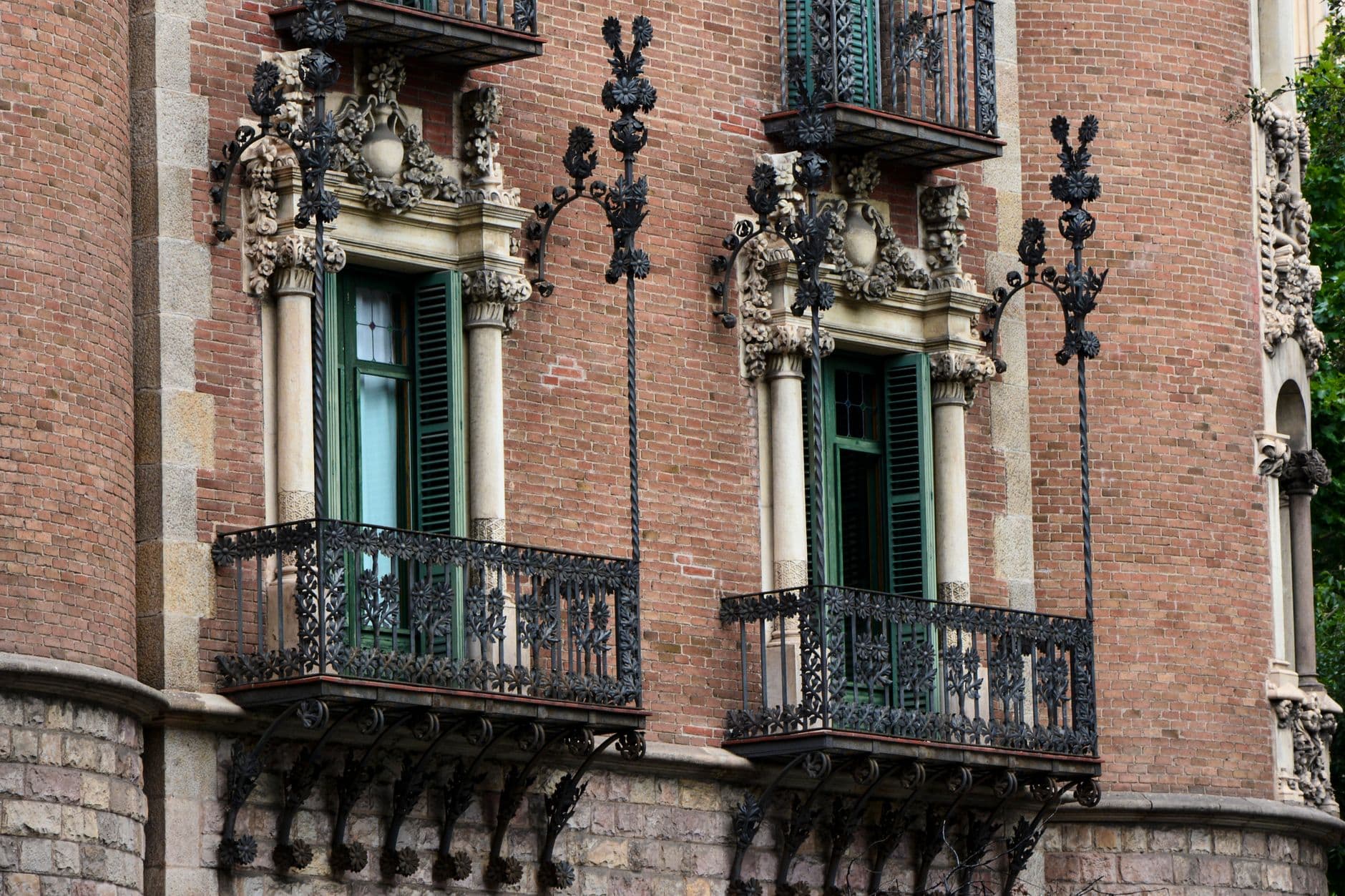 Balcones de hierro forjado y contraventanas verdes en la fachada de ladrillo de un edificio modernista de Barcelona.