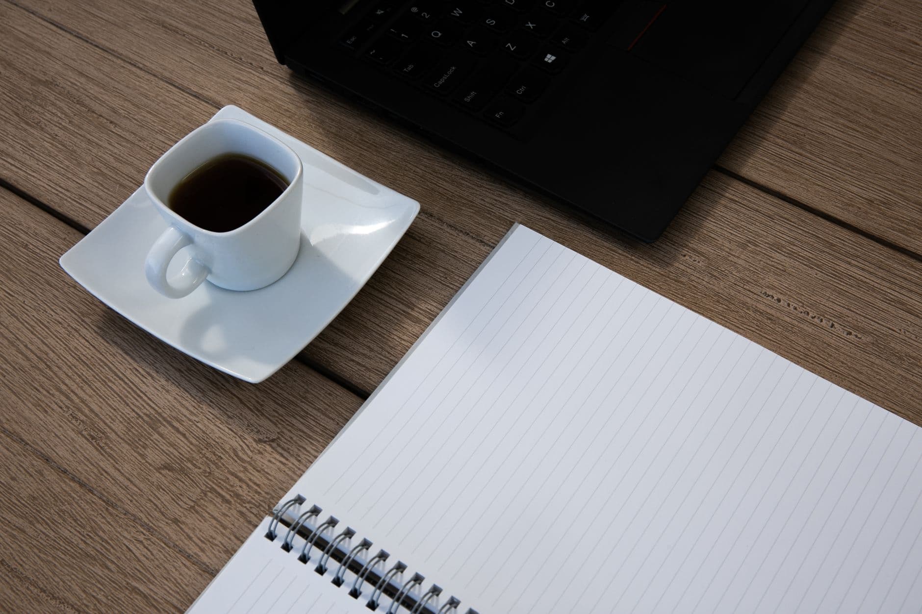 Mesa de madera con un ordenador portatil, una libreta abierta y una taza de cafe