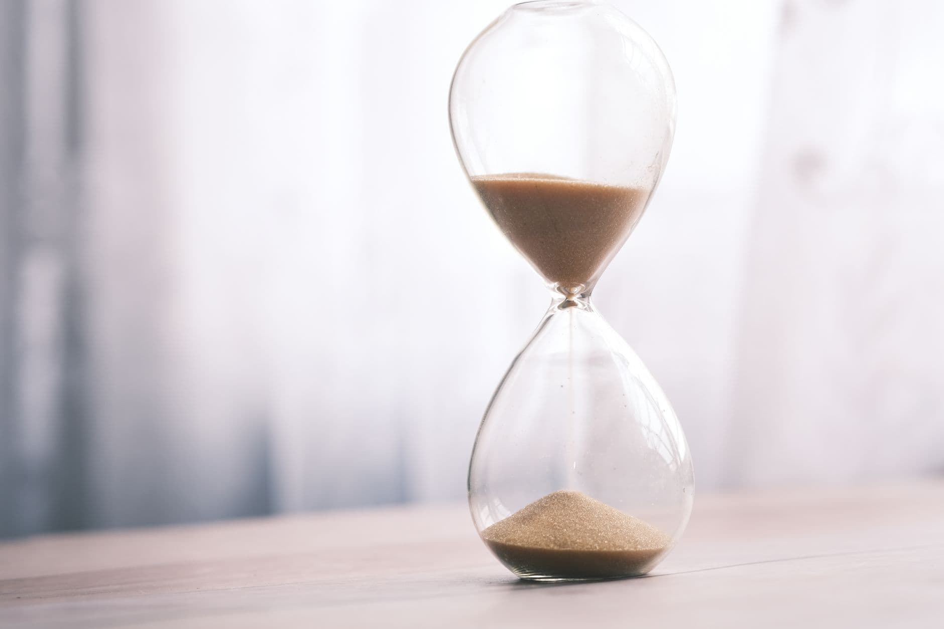 Reloj de arena con la arena cayendo, sobre una mesa clara