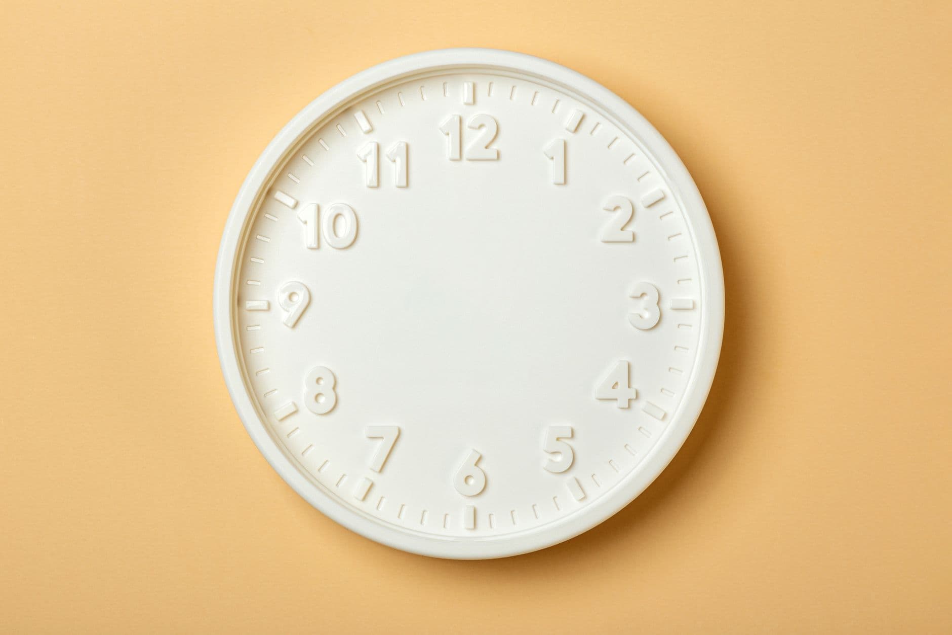 Reloj de pared blanco sin agujas sobre fondo beige.