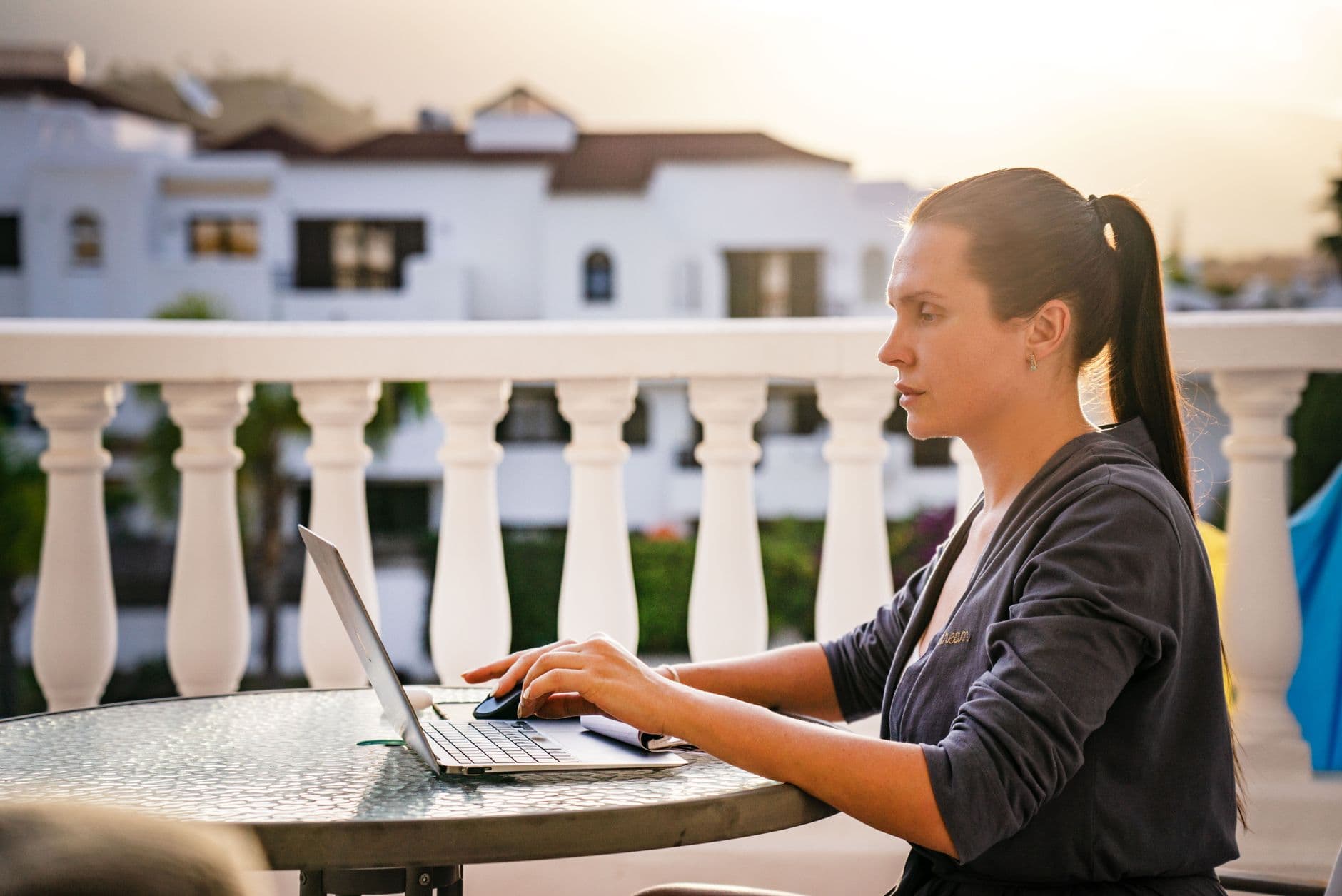 Mujer trabajando con un portatil en la terraza de un edificio blanco al atardecer