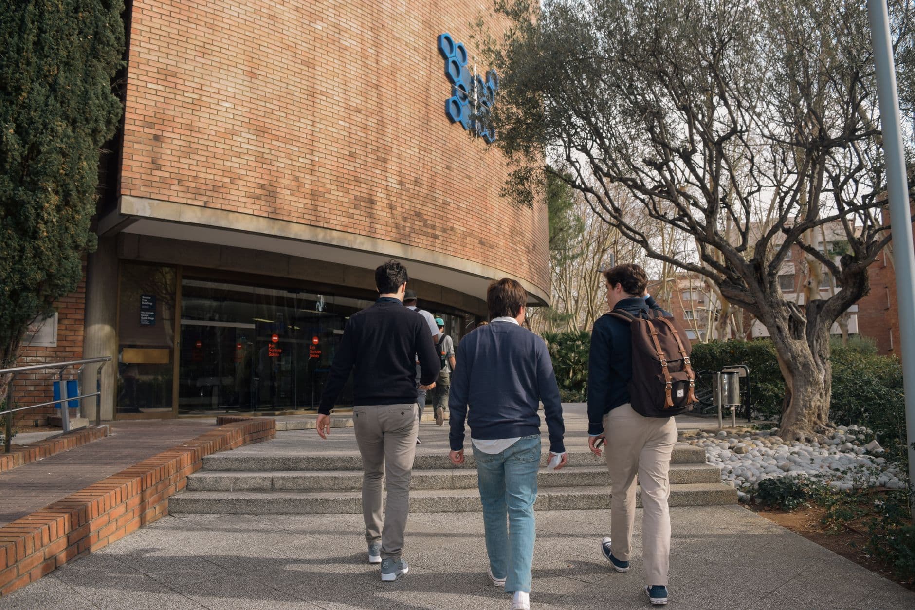 Tres estudiantes suben las escaleras hacia la entrada de un edificio universitario en Barcelona.