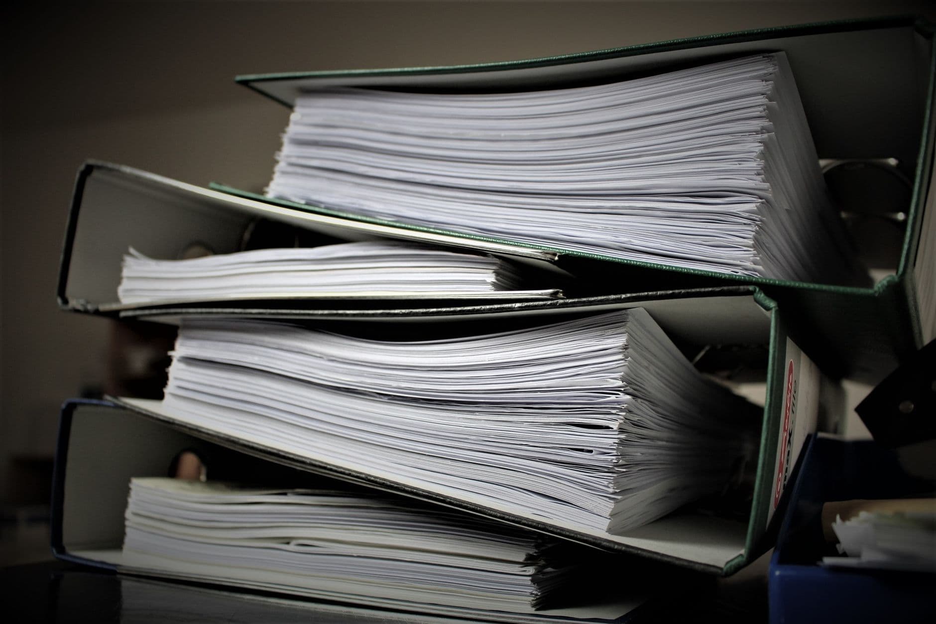 Pila de archivadores abiertos repletos de documentos sobre una mesa de oficina.